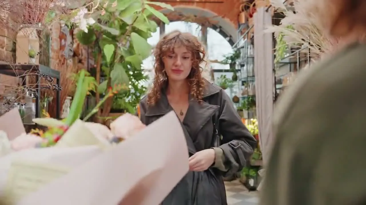 A customer at a flower shop counter surrounded by plants and roses