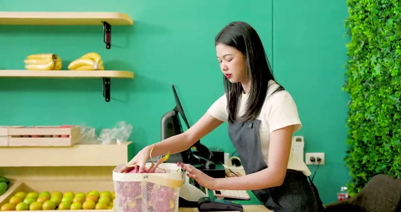 A clerk weighing dragon fruit at a specialty food counter with a POS terminal